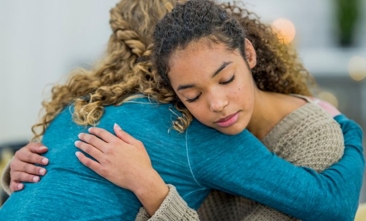 Two teen girls in the Hope Squad are hugging.