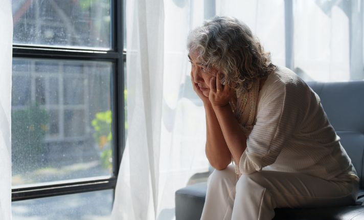 A lonely woman with no social supports sits alone looking out a window.