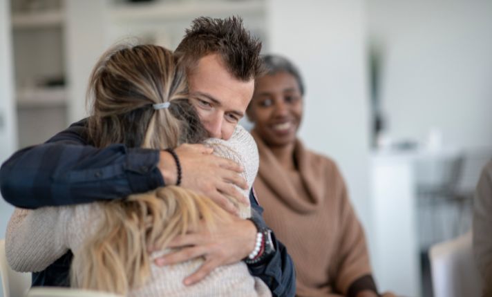A man and a woman at a Utah behavioral health agency hug during group counseling.