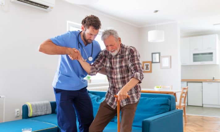A health aide helps an elderly man up as he provides a service in the CalAIM Community Supports Policy Guide.