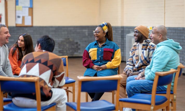 A group of people sit in a circle of chairs as they attend a group from the CalAIM ECM Policy Guide.