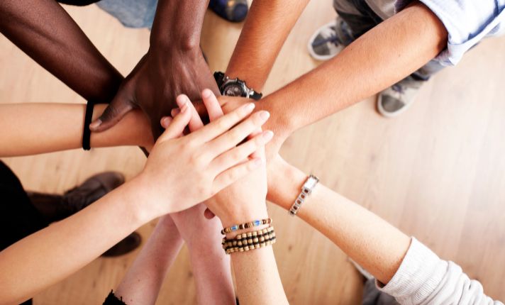 A group of people in a CalAIM ECM program have their hands in on top of each other giving support.