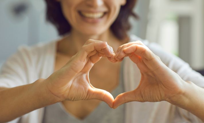A women is making a heart with her hands, representing care with the CalAIM Initiative.
