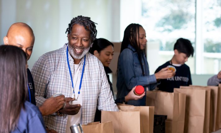 A man and a row of other people have bags of food lined up to give out as part of an enhanced care management program.
